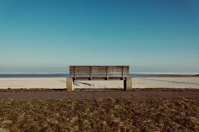 Empty bench on beach against clear sky
