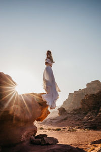 Young woman standing on rock against clear sky