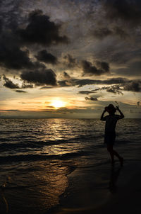 Woman standing on beach against sky during sunset