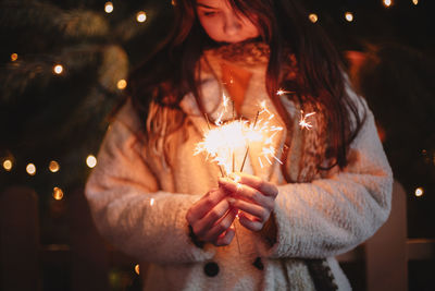 Teenage girl holding sparklers standing by luminous christmas tree