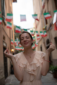 Woman smiling while standing against italian flags hanging amidst buildings