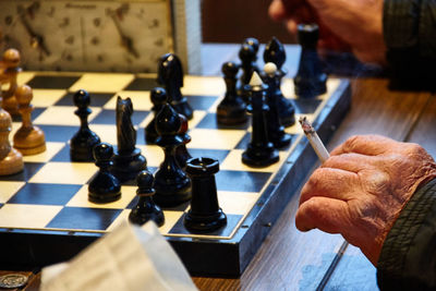 Cropped hand of person holding cigarette by chess board on table