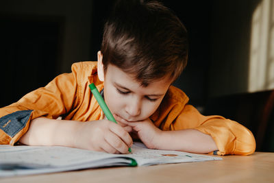 Cute 7 years old child doing his homework sitting by desk. boy writing in notebook.