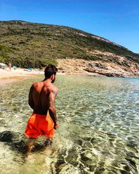 Rear view of shirtless man in sea against sky