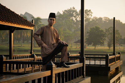 Full length portrait of young man sitting on railing