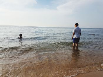 Rear view of boy standing on beach against sky
