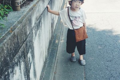 High angle portrait of boy standing on street by retaining wall