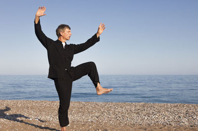 Full length of man doing martial arts on shore at beach