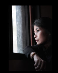 Portrait of a young woman looking through window