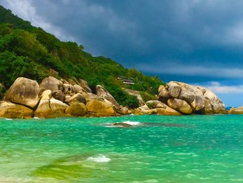 Scenic view of sea by mountain against sky