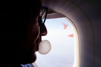 Close-up of man blowing bubble siting in airplane