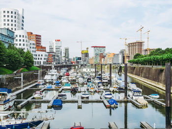 Sailboats moored on canal by buildings in city against sky