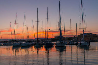 Sailboats moored in harbor at sunset