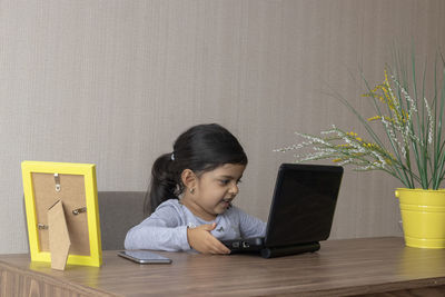 Cute girl using laptop while sitting on table at home