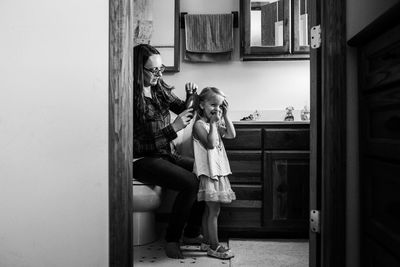 Mother combing hair of daughter at home