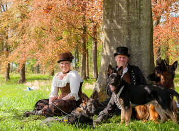 Portrait of happy mature couple sitting with dogs at park during autumn