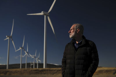 Adult man in winter cloth with modern windmills against blue sky. shot in castilla la mancha, spain