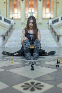 Beautiful girl in black dress plays chess in hall checkered floor