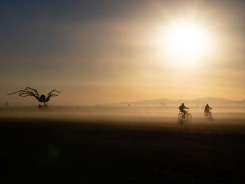 Surreal landscape - people riding motorcycle on the field against sky during sunset