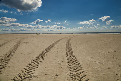 Tire tracks on sand at beach against sky