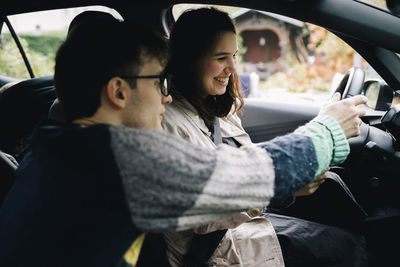 Man holding steering wheel while teaching driving to woman sitting in car