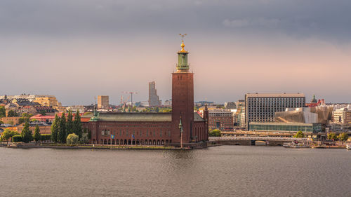 Illuminated buildings by river against sky in city