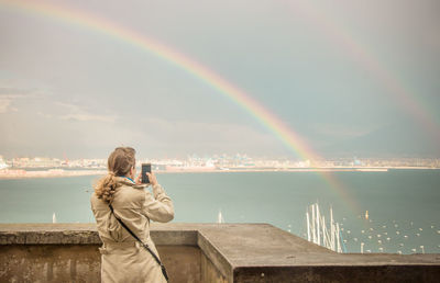 Rear view of man standing on rainbow over sea against sky