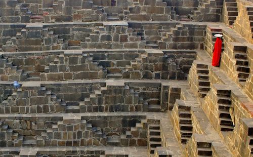 Rear view of woman in orange sari carrying container at chand baori