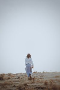 Rear view of woman standing on field against clear sky
