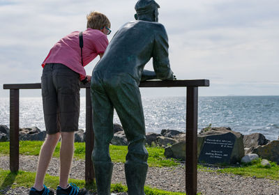 Rear view of men standing by sea against sky