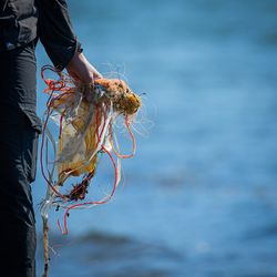 Midsection of person holding fishing net at sea shore