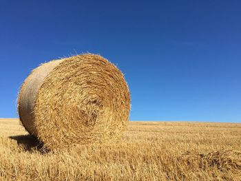 Hay bales on field against clear blue sky