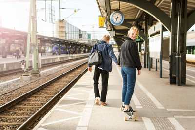 Young man pulling teenage girl on skateboard at railroad station platform