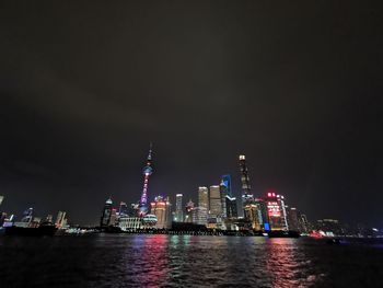 Illuminated buildings by sea against sky at night