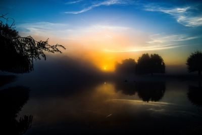 Reflection of silhouette trees in water at sunset