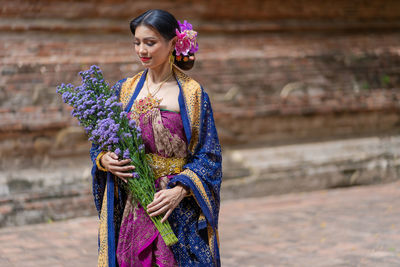 Woman wearing traditional clothing holding bouquet while standing outdoors