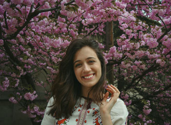 Portrait of smiling young woman with pink flowers against trees