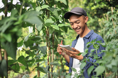 Portrait of smiling young asian farmer man writing on the small notebook. happy young asian farmer at the garden