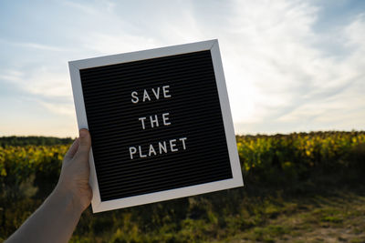 Cropped hand of man holding text against sky