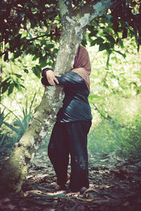 Rear view of woman standing by tree trunk in forest