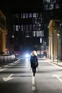Rear view of woman walking on illuminated road at night