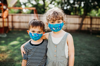 Two young kids standing outside together wearing homemade masks