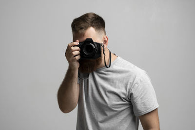 Young man photographing against gray background