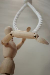 Close-up of wooden figurine by rope against wall