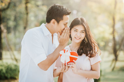 Smiling man whispering into woman ear while giving gift