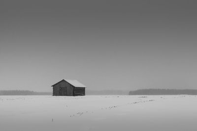 Barn on snow covered field against clear sky