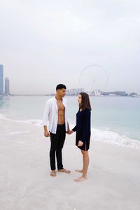 Young beautiful couple standing at beach against sky