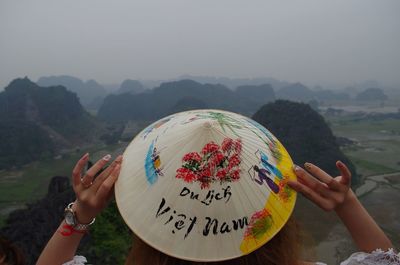 Rear view of woman holding asian style conical hat against mountains