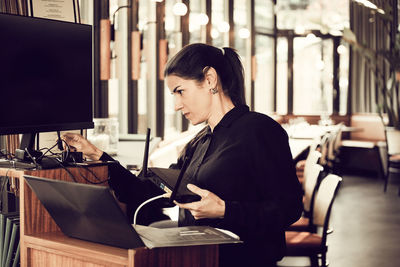 Female owner adjusting wire of computer monitor in cafe