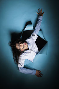 Young woman with arms raised standing against blue background